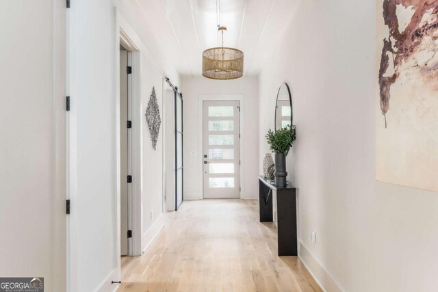 hallway with baseboards, a barn door, and light wood finished floors