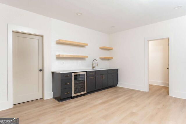 bar with indoor wet bar, beverage cooler, a sink, and light wood-type flooring