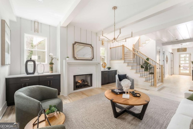 living area featuring a notable chandelier, beam ceiling, a fireplace, light wood-type flooring, and stairway