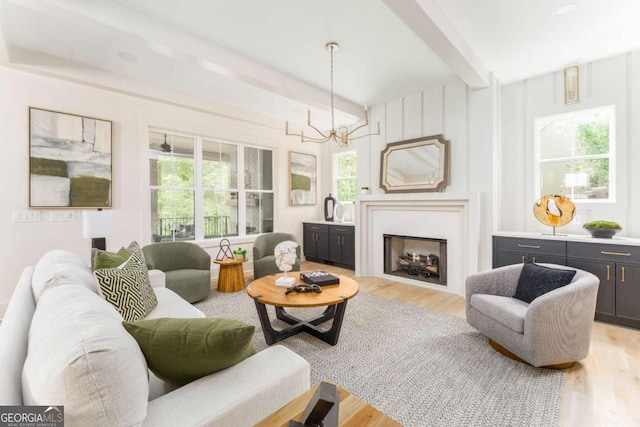 living area with an inviting chandelier, beam ceiling, and light wood-style floors