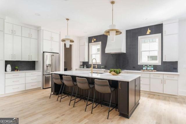 kitchen featuring a kitchen island with sink, tasteful backsplash, high quality fridge, a sink, and light countertops