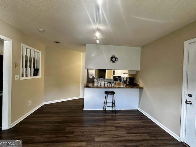 kitchen featuring dark wood-style flooring, dark countertops, a kitchen breakfast bar, a peninsula, and baseboards