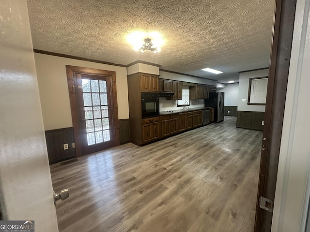 kitchen with wainscoting, a textured ceiling, a sink, light wood finished floors, and appliances with stainless steel finishes