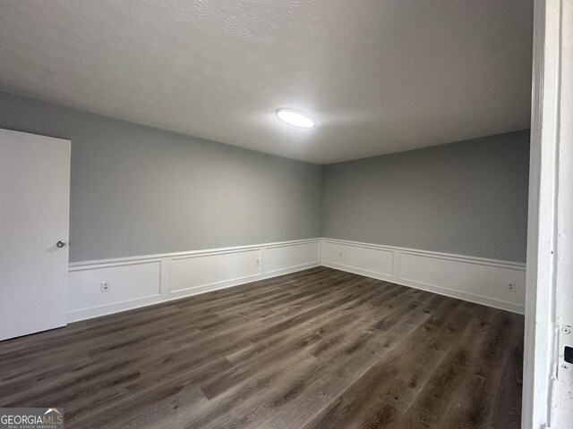 empty room featuring dark wood-type flooring and a wainscoted wall
