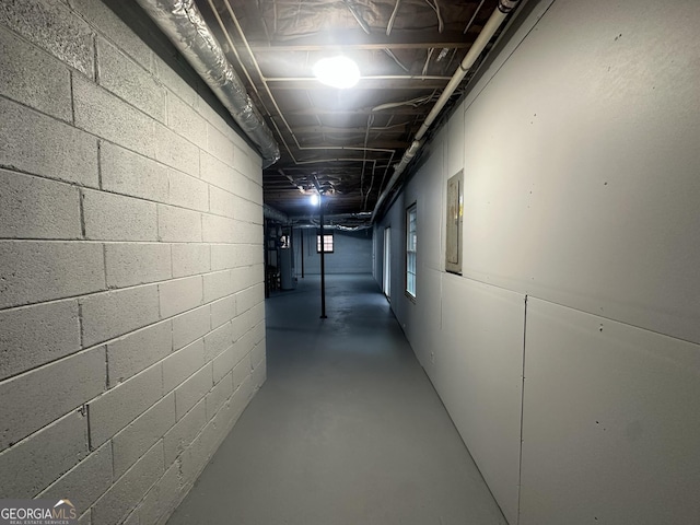 hallway with concrete block wall, finished concrete floors, and electric panel