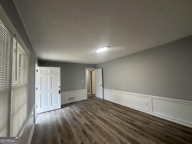 spare room with visible vents, a decorative wall, wood finished floors, a textured ceiling, and a wainscoted wall