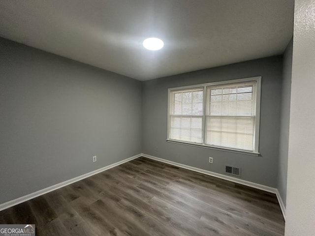 empty room with baseboards, dark wood-type flooring, and visible vents