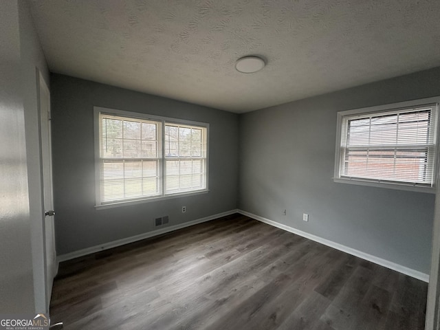 spare room with visible vents, a textured ceiling, dark wood-style flooring, and baseboards