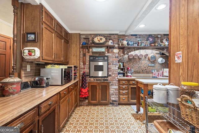 kitchen with brown cabinetry, crown molding, appliances with stainless steel finishes, and beamed ceiling