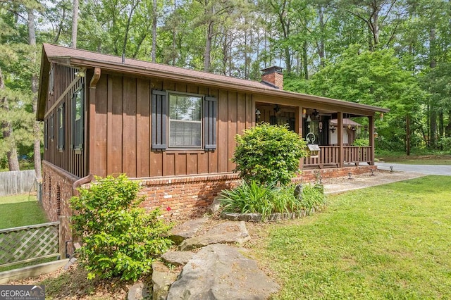 view of front of property featuring board and batten siding, a front yard, a chimney, and a porch