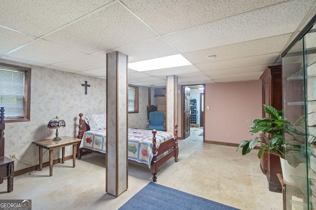 bedroom with baseboards, concrete flooring, and a drop ceiling