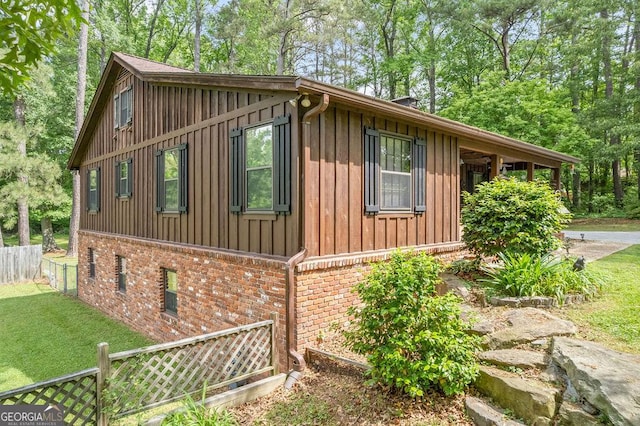 view of side of home featuring fence, board and batten siding, a yard, and brick siding