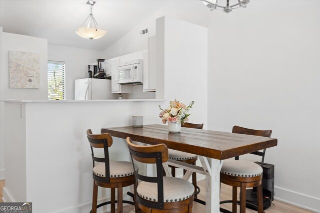dining area with baseboards, visible vents, vaulted ceiling, and light wood-style floors