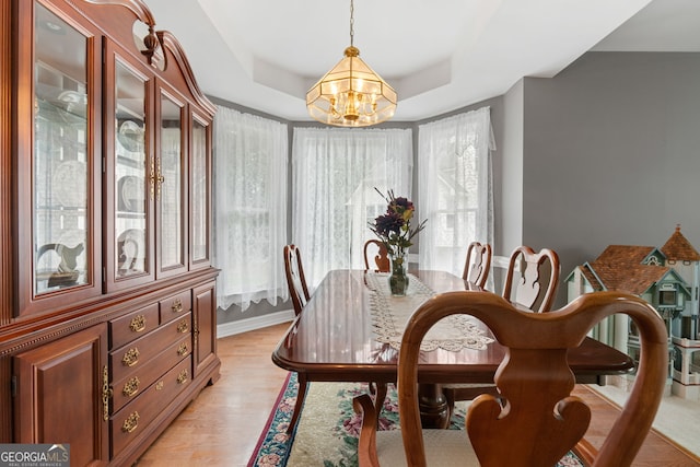 dining area featuring baseboards, light wood-style flooring, a raised ceiling, and a chandelier