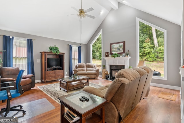 living room with ceiling fan, a fireplace, high vaulted ceiling, light wood-style flooring, and baseboards