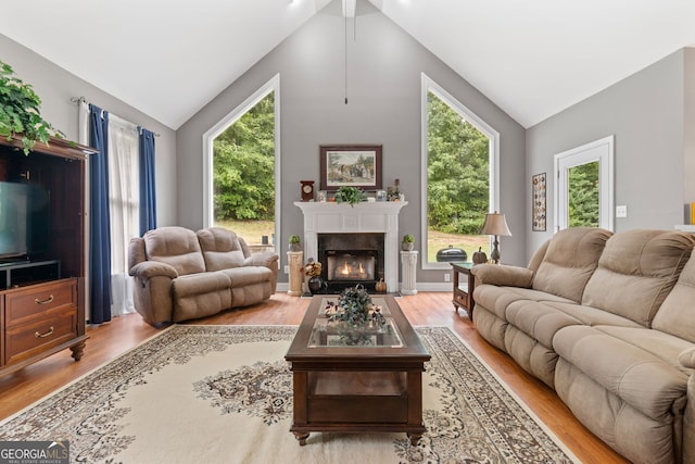 living area featuring a fireplace with flush hearth, vaulted ceiling, light wood-type flooring, and a wealth of natural light