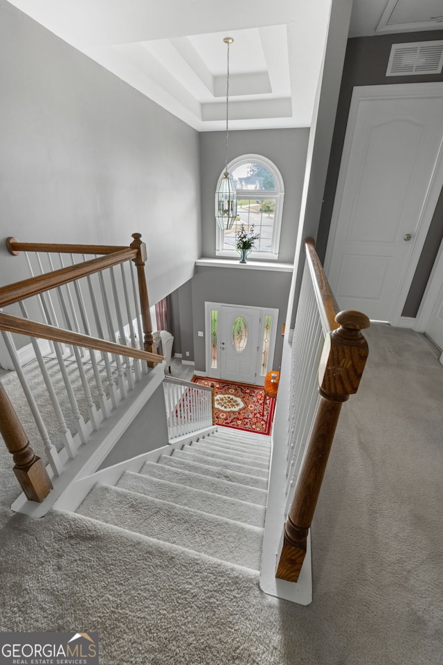 stairs with carpet flooring, visible vents, and a raised ceiling
