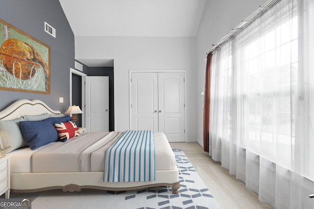 bedroom featuring high vaulted ceiling, a closet, light colored carpet, and visible vents