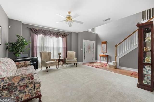 carpeted living room featuring visible vents, a ceiling fan, baseboards, and stairway