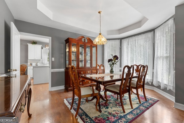 dining space with baseboards, light wood-style flooring, a raised ceiling, and a notable chandelier