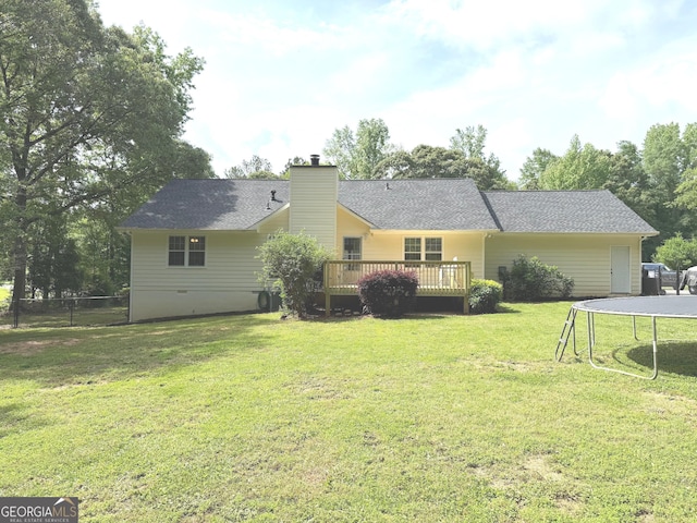 rear view of house with a chimney, a trampoline, a deck, fence, and a yard