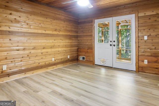 unfurnished room with a ceiling fan, french doors, visible vents, wood finished floors, and wooden walls