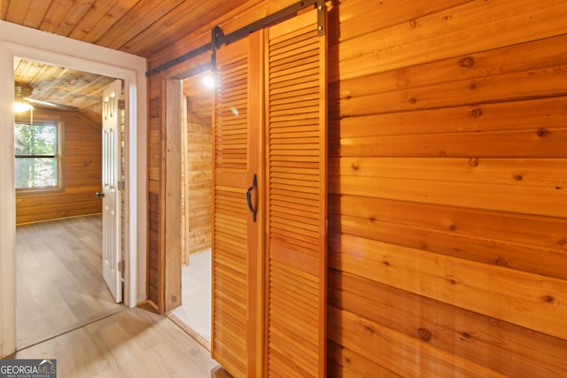 hallway featuring light wood-style flooring, vaulted ceiling, wooden walls, and wood ceiling