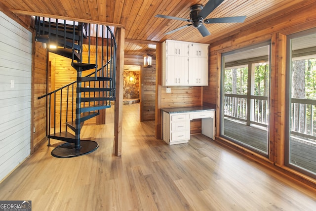 unfurnished office with built in desk, light wood finished floors, wood walls, a ceiling fan, and wooden ceiling