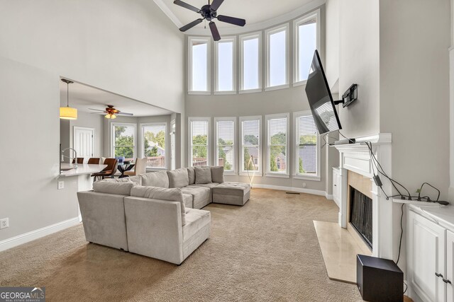 living room with ceiling fan, a towering ceiling, a high end fireplace, and light colored carpet