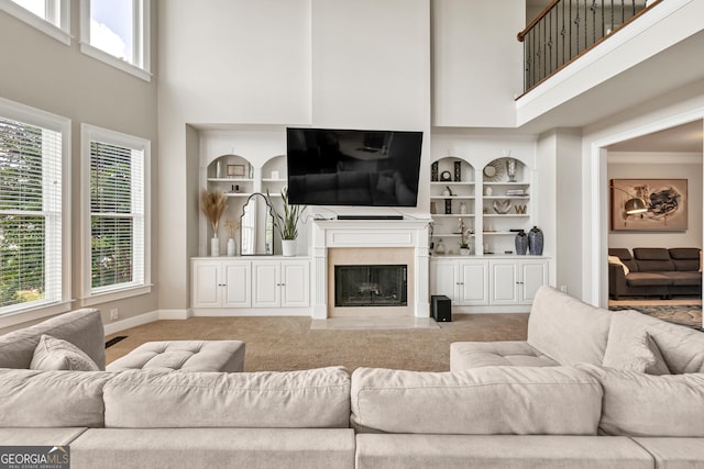 living area with a high ceiling, light carpet, built in shelves, a fireplace, and baseboards