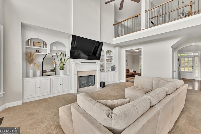 living area featuring built in shelves, carpet floors, ceiling fan, baseboards, and a towering ceiling