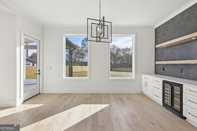 unfurnished dining area with ornamental molding, light wood finished floors, beverage cooler, and a wealth of natural light
