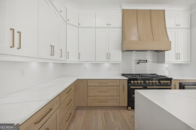 kitchen featuring light stone countertops, light wood-style flooring, double oven range, custom range hood, and tasteful backsplash