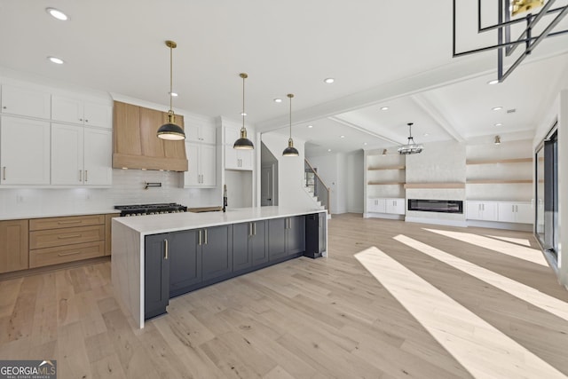 kitchen featuring light wood-style floors, backsplash, a glass covered fireplace, and white cabinetry