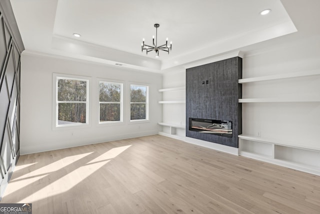 unfurnished living room featuring a fireplace, a chandelier, built in shelves, light wood-type flooring, and a tray ceiling