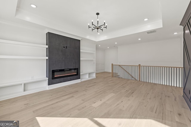 unfurnished living room with an inviting chandelier, a raised ceiling, light wood-style floors, and visible vents