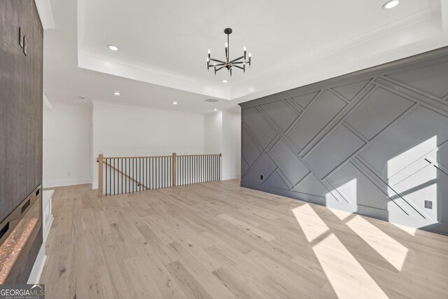 spare room featuring an inviting chandelier, a decorative wall, recessed lighting, light wood-type flooring, and a raised ceiling