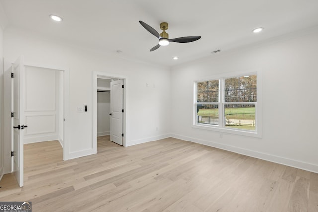 unfurnished bedroom featuring crown molding, visible vents, baseboards, light wood-type flooring, and a spacious closet