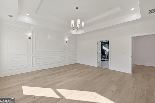 unfurnished dining area featuring crown molding, a raised ceiling, light wood-style flooring, and a notable chandelier