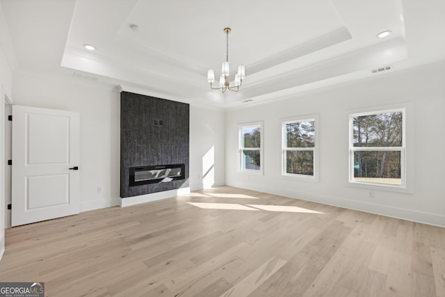 unfurnished living room with visible vents, crown molding, a raised ceiling, light wood-style flooring, and a notable chandelier