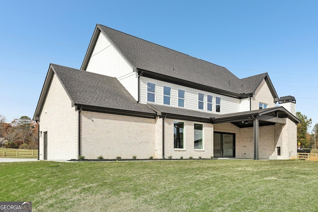 rear view of property featuring a chimney, brick siding, fence, a yard, and a shingled roof