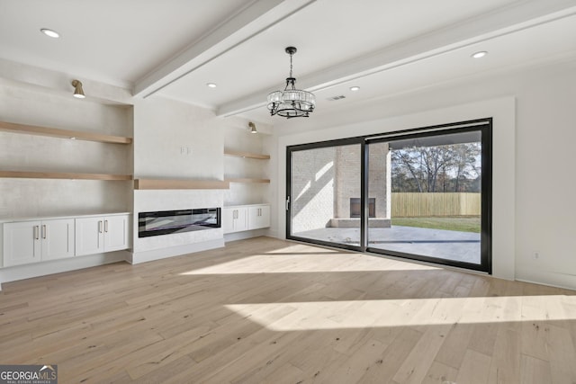 unfurnished living room with a chandelier, a glass covered fireplace, beam ceiling, and light wood-style floors