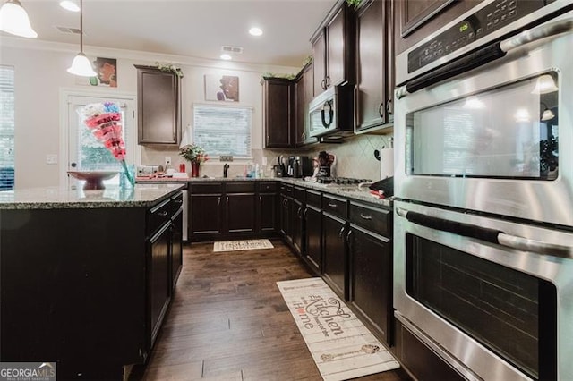 kitchen featuring crown molding, appliances with stainless steel finishes, tasteful backsplash, light stone counters, and dark wood-type flooring