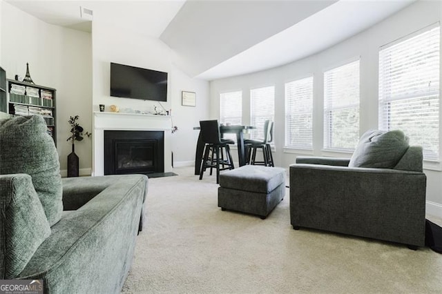 living room featuring carpet floors, a fireplace with flush hearth, baseboards, and lofted ceiling