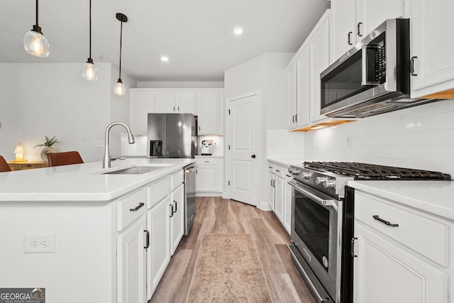 kitchen with appliances with stainless steel finishes, a sink, decorative light fixtures, decorative backsplash, and light wood-type flooring