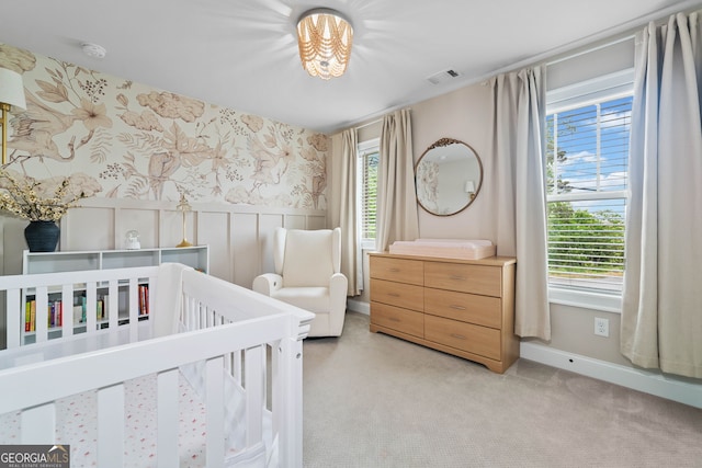 bedroom with a nursery area, light colored carpet, wainscoting, wallpapered walls, and visible vents