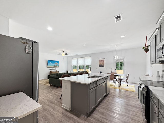 kitchen with visible vents, a kitchen island with sink, gray cabinets, a sink, and stainless steel appliances