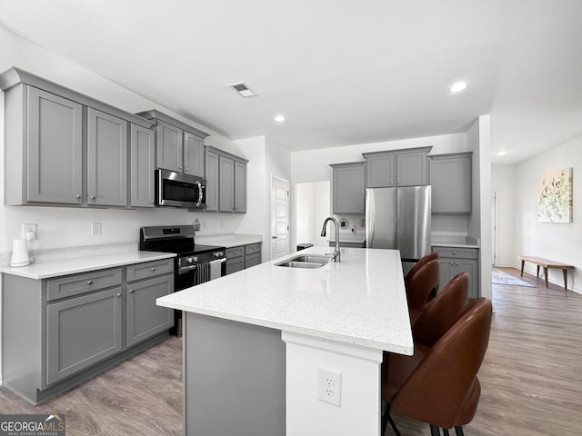 kitchen with gray cabinets, a kitchen bar, appliances with stainless steel finishes, a sink, and an island with sink