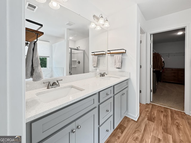 bathroom featuring a sink, wood finished floors, a spacious closet, and a shower stall