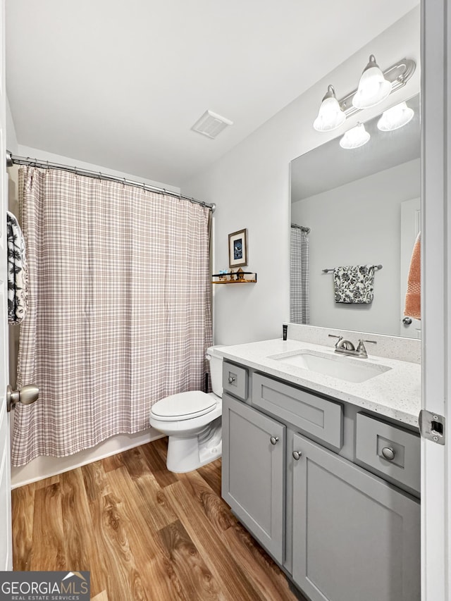 bathroom with shower / tub combo with curtain, vanity, toilet, wood finished floors, and visible vents